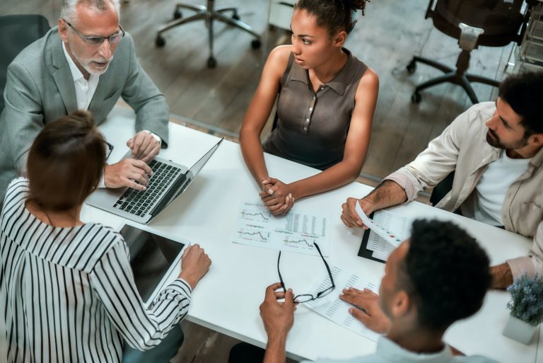 Top view of multicultural team discussing business while sitting at the office table together